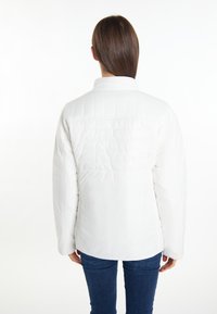 Jachetă albă izolată cu un design capitonat. Are un guler înalt și mâneci lungi. Este purtată cu blugi bleumarin.