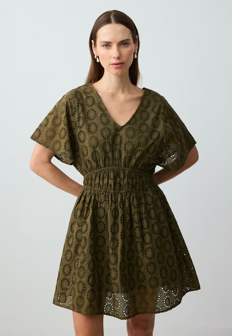 Olivegrünes Kleid mit V-Ausschnitt, kurzen Ärmeln und elastischem Bund. Verfügt über ausgeschnittene Blumenmuster und einen ausgestellten Rock.