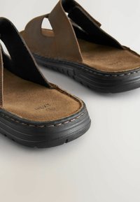 Sandales en cuir marron avec semelles en caoutchouc noires, présentant un design à deux brides, des accents découpés et des détails cousus le long des bords.