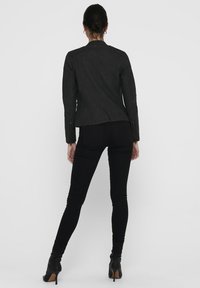 Zwarte leren motorjack met gewatteerde schouderdetails, aansluitend design en ritsaccenten, gecombineerd met zwarte skinny broeken en haklaarzen.