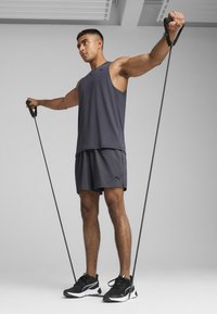 Γκρι αθλητικό τοπ και σορτς, με μαύρες λάστιχες αντοχής· μαύρα και λευκά παπούτσια, σε ουδέτερο φόντο.