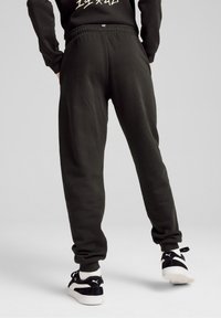 Pantalones de chándal verde oscuro con cintura elástica, piernas ajustadas y una textura suave. Llevados con zapatillas negras y blancas.