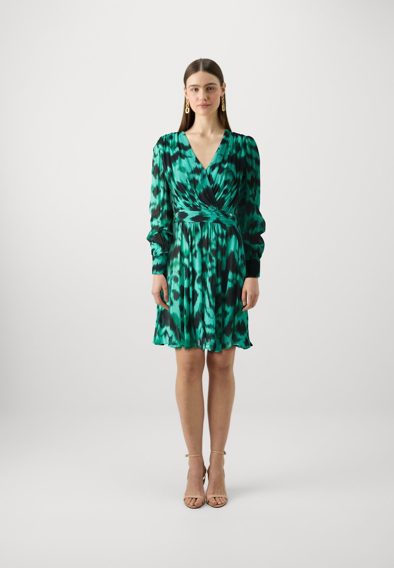 Robe verte avec un motif abstrait noir et turquoise, décolleté en V, manches longues, taille cintrée et ourlet fluide. Finition en tissu lisse.