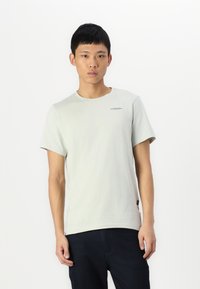 Lichtgrijze t-shirt met korte mouwen en een ronde halslijn, subtiel logo op de borst. Gemaakt van katoen, relaxte pasvorm, gecombineerd met donkere jeans.