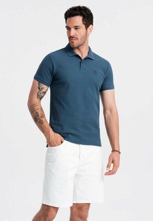 Mørkeblå polo med krave, korte ærmer og logo-detalje. Sammen med hvide shorts. Fremstillet i bomuldsstof med glat tekstur.
