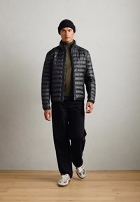 Sort puffet jakke, grøn turtleneck, sorte bukser og grå sneakers. Enkel design, glat tekstur og lynlåse på jakken.