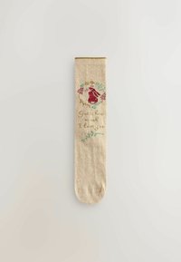 Beige strumpa med stickad röd kanin-design, omgiven av gröna blad och gula blommor. Texten lyder: "Gissa hur mycket jag älskar dig."