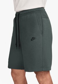 Mörkgröna Nike-shorts i texturerad tygkvalitet, med elastisk midja, svarta dragsnören och sidofickor. Nike-logotypen tryckt i svart.