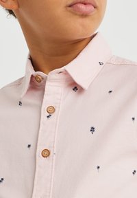 Ljusrosa knäppskjorta med små broderade marinblå palmträd, krage och bruna knappar. Tillverkad av bomull med en slät textur.