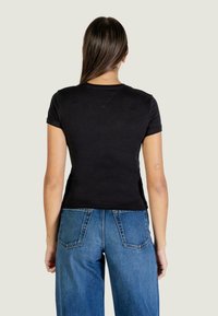 Maglietta nera a maniche corte con un design aderente, realizzata in tessuto di cotone liscio. La vista posteriore mostra il dettaglio del collo e le maniche semplici.