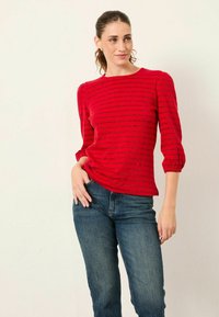Rotes Strickoberteil mit horizontalen Streifen, Dreiviertelärmeln und gerippter Textur, kombiniert mit blauen Jeans.