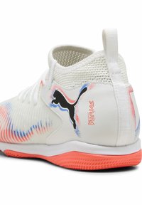 Chaussure de sport blanche avec accents rouges et bleus, logo Puma noir, texte rouge "Play Free Future", lacets blancs et semelle texturée rouge.
