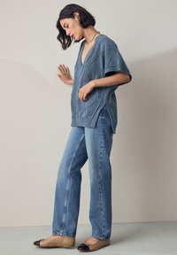 Top albastru tricotat cu gât în V și modele de dantelă, asortat cu blugi drepti, de culoare albastru deschis, și balerini maro deschis cu vârful negru.