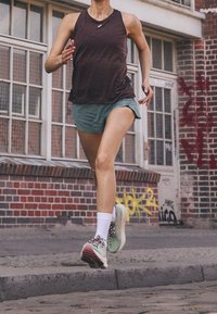 Sportovní oblečení se skládá z bezramínkového tmavě fialového tílka a světlezelených kraťasů. Doplněno bílými kotníkovými ponožkami a barevnými běžeckými botami.