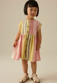 Robe rayée colorée avec des teintes jaunes, roses et blanches, dotée d'un bouton à l'avant et d'une jupe évasée. Des sandales avec des accents floraux complètent le look.