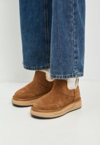 Brune ruskinds ankle boots med en beige gummisål, der har en blød for, syninger og en rund tå. Båret med blå denim jeans.