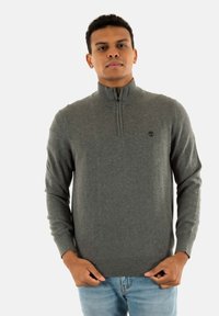 Maglione grigio con zip e colletto alto, realizzato in tessuto morbido. Presenta polsini e orlo a coste, e un piccolo logo sul petto.