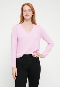 Ανοιχτό ροζ, πουλόβερ με μακριά μανίκια και V-λαιμόκοψη από απαλό ύφασμα, σε συνδυασμό με μαύρο, ψηλόμεσο τζιν. Λεπτή υφή, casual εφαρμογή.