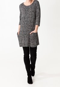 Túnica estampada en blanco y negro con mangas de tres cuartos y bolsillos frontales, combinada con pantalones negros ajustados y botas de tobillo.