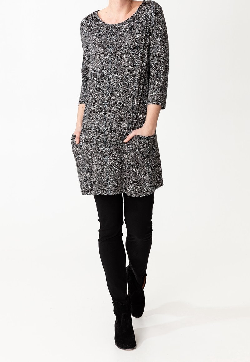 Túnica estampada en blanco y negro con mangas de tres cuartos y bolsillos frontales, combinada con pantalones negros ajustados y botas de tobillo.