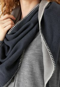 Grande écharpe tricotée avec un jeu de couleurs bleu marine et gris, bordée de fines coutures blanches et une texture de tissu douce.