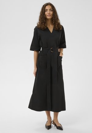 Čierne šaty dĺžky po členky s výstrihom do V a krátkymi rukávmi, v páse zoštíhlené látkovým opaskom a s dvoma bočnými vreckami.