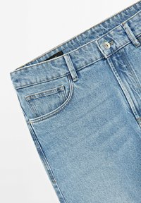 Světle modré džíny ze denimu, s klasickým střihem, přední kapsou a kovovým zapínáním na knoflík. Tkanina má jemnou, opotřebovanou strukturu.