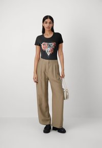 T-shirt noir à manches courtes avec motif floral et texte "GUESS" ; associé à un pantalon beige ample et des chaussures à plateforme noires ; sac à main blanc.