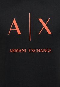 Μαύρο ύφασμα με έντονα πορτοκαλί γράμματα "A | X" πάνω από το κείμενο "ARMANI EXCHANGE" κεντραρισμένα στην επιφάνεια.