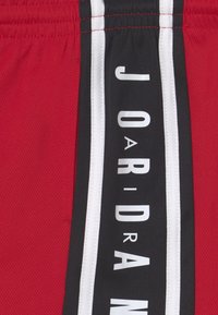 Röda sportshorts med svarta sidostråkar som har vit text som stavar "JORDAN." Tillverkade av meshmaterial för god andningsförmåga.