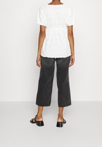 White eyelet blouse with short sleeves, gathered waist, and slight texture, paired with black wide-leg jeans and black block-heeled sandals.