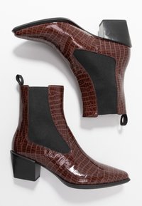 Botas de tobillo de charol marrón con un patrón de cocodrilo, paneles laterales elásticos y un tacón cuadrado. Superficie texturizada y detalle de lengüeta.