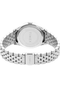 Montre en acier inoxydable argenté avec un bracelet à maillons, un cadran rond et un design lisse et minimaliste. Elle possède une fermeture et le nom de la marque gravé.