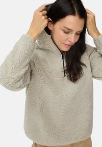Fleece pullover in lichtbeige met een gestructureerd, pluizig oppervlak. Voorzien van een halfrits aan de voorkant en een verstelbare capuchon.