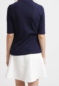 Mörkblå pikétröja med korta ärmar, tillsammans med en vit texturerad kjol med en utställd design och ett komplext geometriskt mönster.