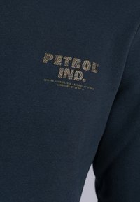 Sudadera de algodón azul oscuro con un logo texturizado impreso en beige en el pecho, con coordenadas geográficas debajo.