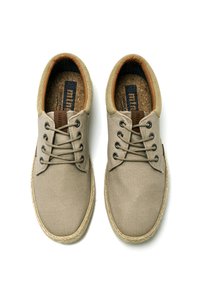 Zapatos de lona beige con acentos marrones, cordones planos y una suela texturizada. Presentan una plantilla de corcho y detalles cosidos alrededor del borde.