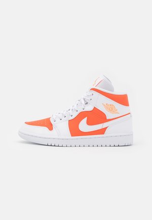 Zapatilla blanca y naranja brillante de caña alta con el logo de Nike swoosh y el logo de las alas de Air Jordan, vista lateral sobre un fondo blanco liso.