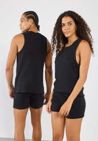 Camisetas sin mangas negras de canalé combinadas con pantalones cortos a juego, con un diseño ajustado y un corte sin mangas. La tela tiene un aspecto suave y texturizado.