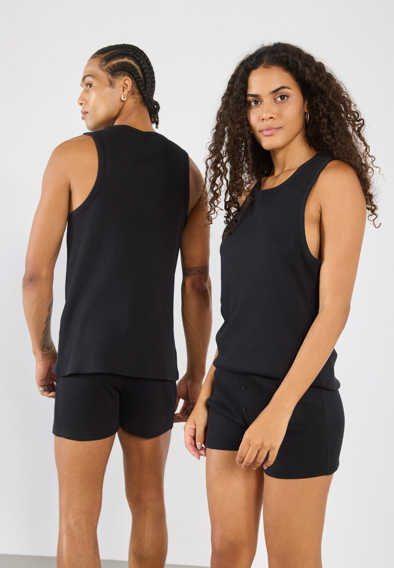 Camisetas sin mangas negras de canalé combinadas con pantalones cortos a juego, con un diseño ajustado y un corte sin mangas. La tela tiene un aspecto suave y texturizado.