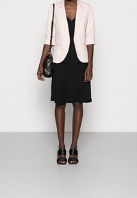 Světle růžový blazer přes černý top a černou sukni. Černé páskové podpatky. Černá prošívaná kabelka. Hladká látka a přizpůsobený design.