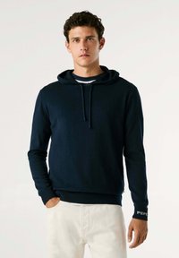 Mornarško modra kapuca z dolgimi rokavi in vrvico, narejena iz mehkega materiala; ima rebraste manšete in akcent logotipa na rokavu.