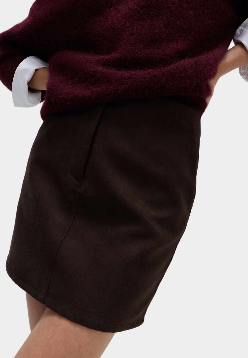 Bordeaux fuzzy sweater over een witte blouse, gecombineerd met een aansluitende donkerbruine rok met zijzakken en een gladde textuur.