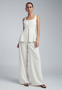 Weißes Leinen-Peplum-Top mit quadratischem Ausschnitt und Knöpfen vorne, kombiniert mit weit geschnittenen Hosen aus dem gleichen Stoff, mit dezenter Textur.