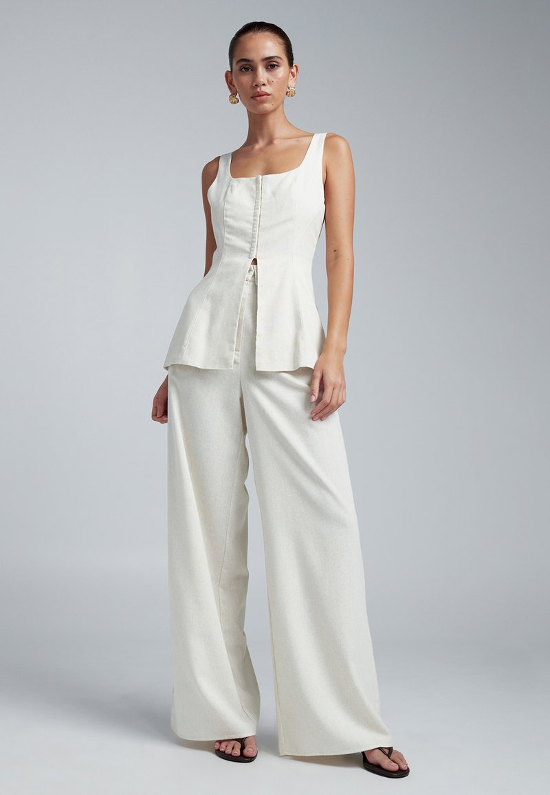 Weißes Leinen-Peplum-Top mit quadratischem Ausschnitt und Knöpfen vorne, kombiniert mit weit geschnittenen Hosen aus dem gleichen Stoff, mit dezenter Textur.