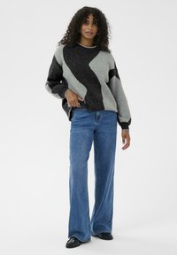 Gray and black patterned sweater with a wide silhouette, paired with light blue flared jeans and black shoes, set against a white background.