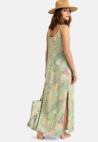 Abito maxi floreale in verde chiaro con spacchi laterali, caratterizzato da motivi tropicali in rosa e giallo. Accompagnato da una borsa a spalla coordinata.