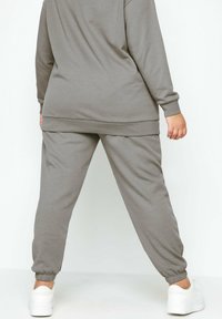 Grijze sweatshirt en jogger set, gemaakt van zachte stof. Kenmerkt rib gebreide manchetten, elastische tailleband en een ontspannen pasvorm. Witte sneakers zichtbaar.