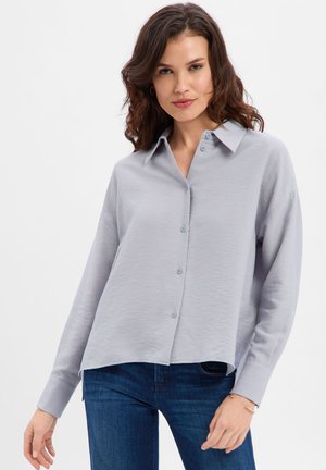 Light gray long-sleeve button-up shirt with a collar, relaxed fit, and textured fabric. Paired with dark blue jeans.