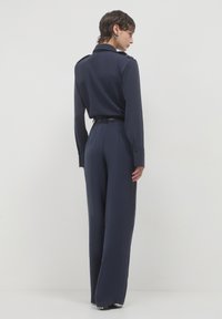 Chemise boutonnière bleu marine à manches longues et épaulettes, associée à un pantalon large taille haute. Coupe ajustée, tissu lisse.